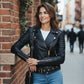 Woman wearing a Scarlett Stitch black faux leather biker jacket with gold hardware and belted waist on a city street.