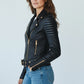 Woman wearing a Scarlett Stitch black faux leather biker jacket with gold hardware, ribbed shoulders, and belt.