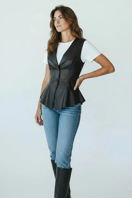 Scarlett Stitch black faux leather peplum vest with notched lapel and single-button closure, worn over a white tee and jeans.