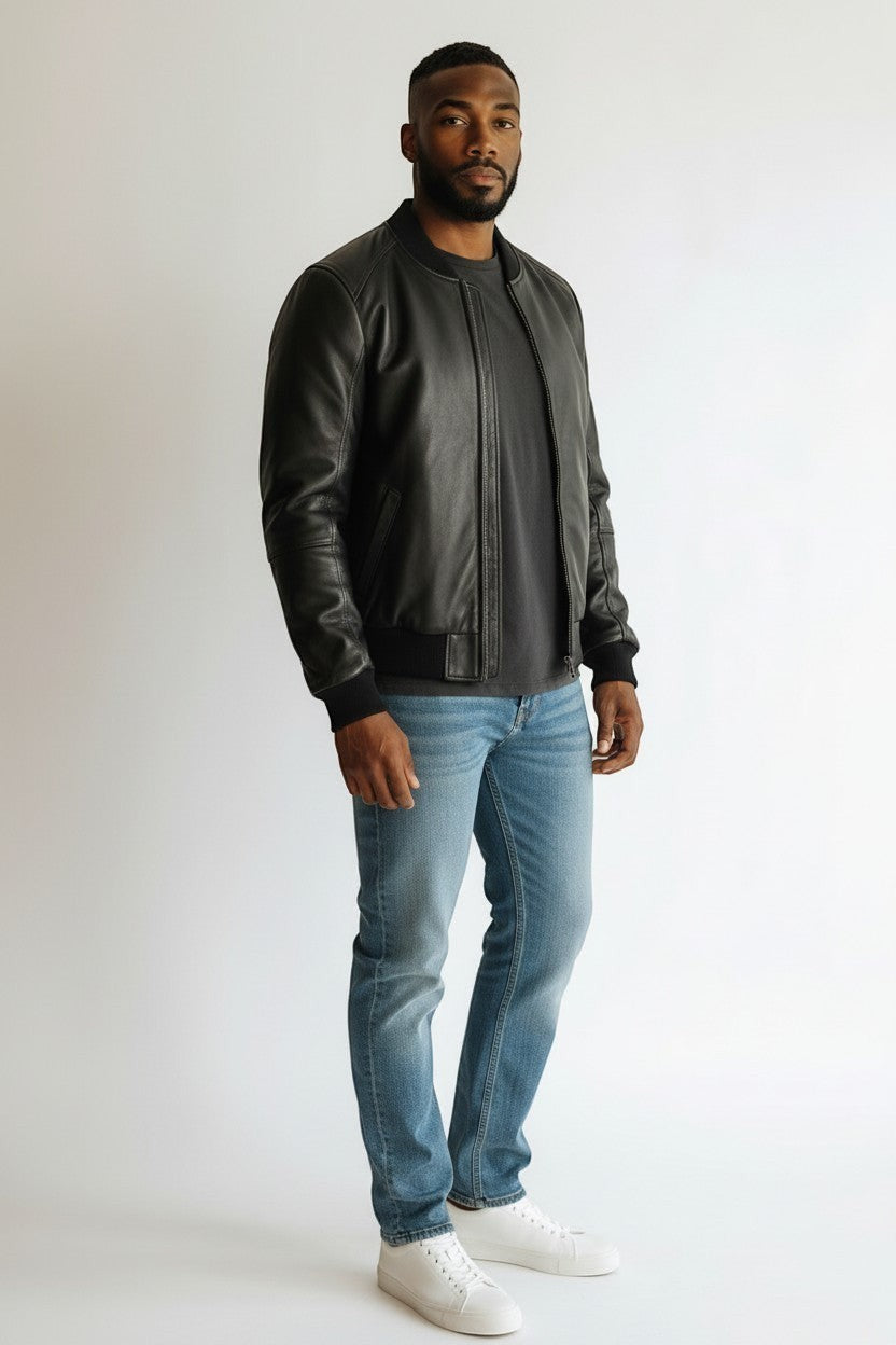 Scarlett Stitch black leather bomber jacket on a man wearing a grey t-shirt and blue jeans. Features ribbed collar, cuffs, and hem.