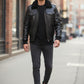 A man wearing a black Scarlett Stitch leather bomber jacket with a faux-shearling collar, black shirt, and grey jeans.