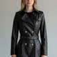 Model wearing a black Scarlett Stitch double-breasted leather trench jacket with silver buttons and a waist belt.