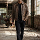 Scarlett Stitch men's brown distressed leather bomber jacket worn by a model in an industrial setting.
