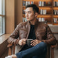 Scarlett Stitch brown faux leather bomber jacket with stand collar, zippered front, and ribbed cuffs. Model wears it with jeans and a t-shirt.