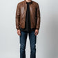 Scarlett Stitch brown faux leather bomber jacket with stand collar, zippered front, and ribbed cuffs. Model wears jeans and t-shirt.