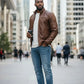 Scarlett Stitch men's brown faux leather bomber jacket with quilted shoulders and zip pockets. Model is wearing jeans and a white t-shirt.