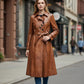 Scarlett Stitch brown faux leather belted trench coat with notched lapel and dark buttons. Model wears jeans and sneakers.