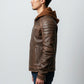 Scarlett Stitch men's brown leather jacket with a hood, quilted shoulders, and zippered pockets, side profile view.