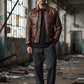 Scarlett Stitch Men's distressed brown leather bomber jacket with shirt collar, zipper, and ribbed cuffs. Model wears it with a black t-shirt and grey trousers.