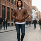 Scarlett Stitch men's distressed brown leather hooded bomber jacket with zip-up front and ribbed cuffs.