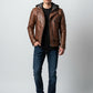 Scarlett Stitch men's brown distressed leather motorcycle jacket with a grey knit hood, worn with jeans and sneakers.