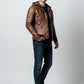 Scarlett Stitch men's brown distressed leather motorcycle jacket with a grey knit hood, worn with jeans and sneakers.