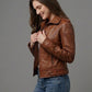 Scarlett Stitch Women's brown leather motorcycle jacket with zippered cuffs, epaulets, and buckle tabs.