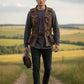 Man wearing a Scarlett Stitch brown distressed leather utility vest with pockets and belt in a rural field.