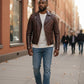 Scarlett Stitch men's brown quilted leather motorcycle jacket with asymmetrical zip worn by a man on a city street.