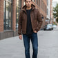 Scarlett Stitch men's brown suede hooded bomber jacket with zip pockets and epaulets, worn with jeans and sneakers.