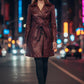 Scarlett Stitch burgundy faux leather double-breasted belted trench coat worn by a woman on a city street at night.