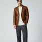 Model wearing a Scarlett Stitch cognac brown leather blazer with notch lapels, white t-shirt, and grey trousers.