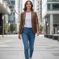 Scarlett Stitch cognac brown leather blazer worn by a woman with a white tee, blue jeans, and sneakers in the city.
