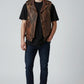 Model wearing a Scarlett Stitch brown distressed leather biker vest with snap buttons and zip pockets over a black tee.