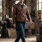 Scarlett Stitch distressed brown leather motorcycle jacket with asymmetrical zip, worn by a man in an industrial space.