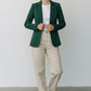 Scarlett Stitch women's forest green tailored blazer jacket with single-button closure and pockets, worn over a white t-shirt and beige pants.