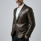 Man wearing a Scarlett Stitch dark brown leather blazer with a white shirt and black trousers against a grey background