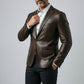 Man wearing a Scarlett Stitch dark brown leather blazer with a white shirt and black trousers against a grey backdrop.