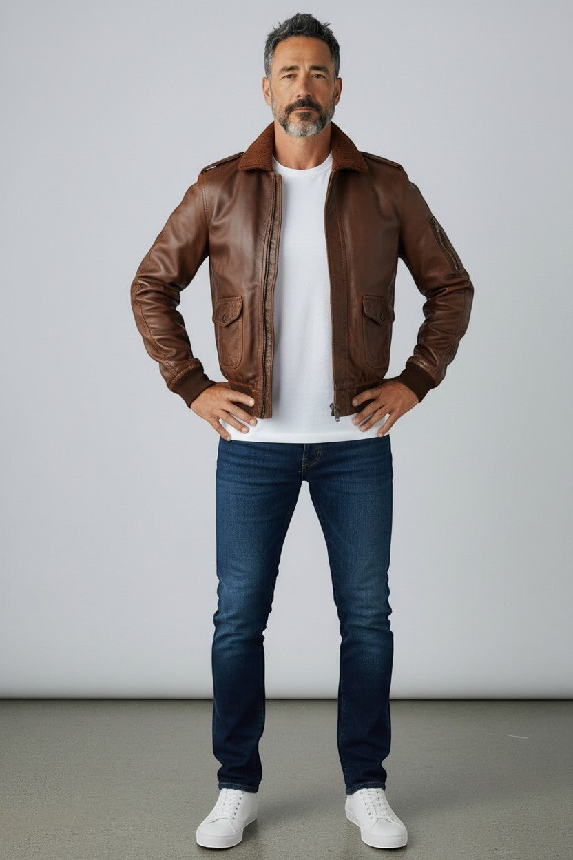 Scarlett Stitch Men's brown leather bomber jacket with ribbed collar, cuffs, and hem. Features dual chest pockets and side pockets.