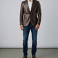 Man wearing a Scarlett Stitch dark brown leather blazer with a white shirt and blue jeans against a grey background.