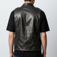 Back view of a man wearing a Scarlett Stitch distressed rust brown leather military vest over a black t-shirt.