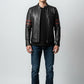 A man wearing a Scarlett Stitch black leather racer jacket with red sleeve stripes, dark jeans, and white sneakers.