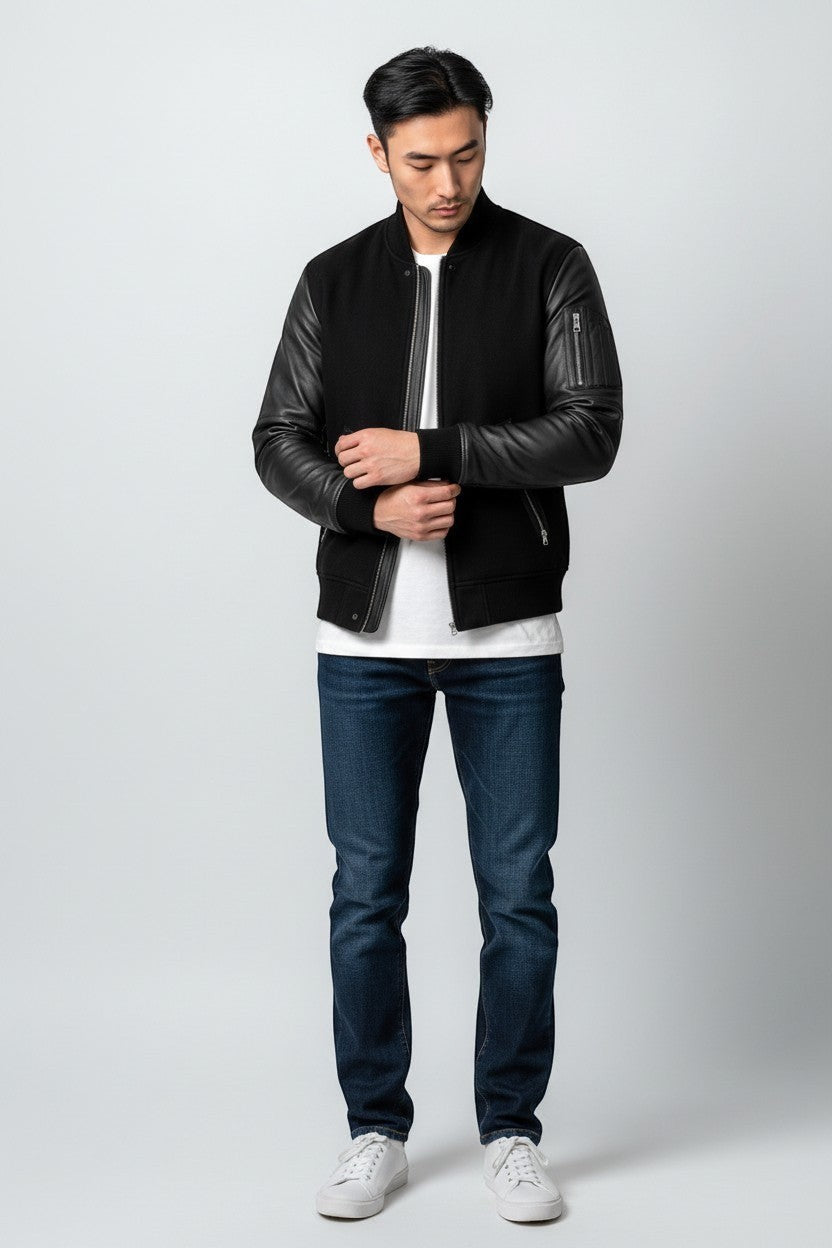 Scarlett Stitch Men's black bomber jacket with genuine leather sleeves, ribbed collar, cuffs, and hem. Features zippered pockets.