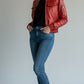 Scarlett Stitch red leather bomber jacket with zippered pockets and ribbed trim, worn by a woman with jeans and sneakers.