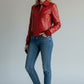 Scarlett Stitch women's red leather bomber jacket with zip-front, folded collar, and ribbed cuffs. Model wears jeans and sneakers.