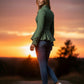 Scarlett Stitch sage green tailored peplum jacket with button detail on cuffs, worn by a woman with jeans at sunset.