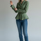 Scarlett Stitch sage green tailored peplum jacket with button detail and bow cuffs, worn by a model with blue jeans.