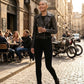 Scarlett Stitch black leather biker jacket with silver studs, worn by a model on a cobblestone street.