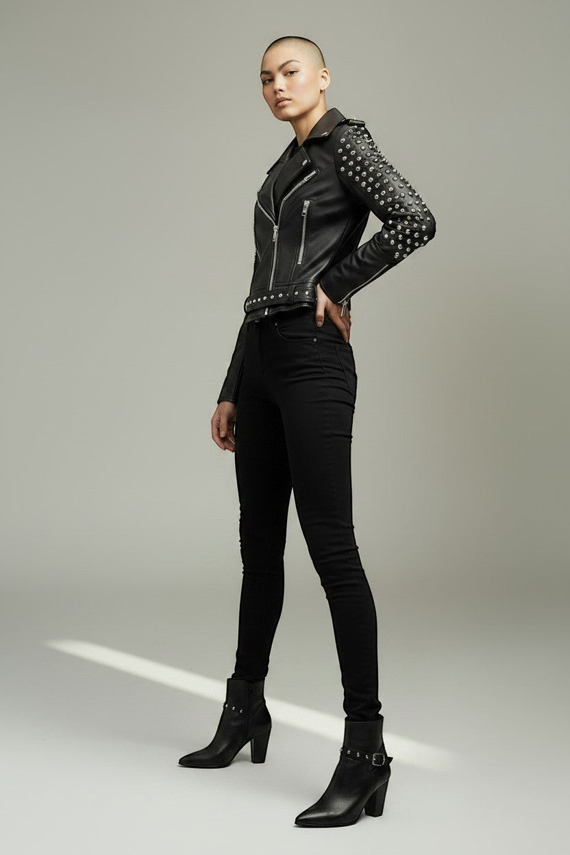 Model wearing a Scarlett Stitch black leather biker jacket with silver stud embellishments, zippers, and waist belt.