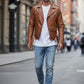 Man wearing a Scarlett Stitch tan leather biker jacket with asymmetrical zip, belt, and epaulets on a city street.