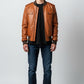 Scarlett Stitch men's tan genuine leather bomber jacket with ribbed collar, cuffs, and hem. Features zip front, chest flap pockets, and side welt pockets.
