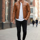 Scarlett Stitch tan leather cafe racer jacket with zippered pockets worn by a man in black jeans and white sneakers.