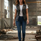 Scarlett Stitch Women's black faux leather motorcycle vest with lapel collar, zipper, and buckle straps. Model wears it over a white t-shirt and blue jeans.