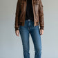Scarlett Stitch Women's distressed brown leather bomber jacket with sherpa collar and zippered pockets.