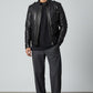 Scarlett Stitch black faux leather bomber jacket for men with stand collar and zippered pockets. Model wears it with a black t-shirt and grey trousers.