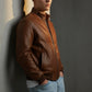 Scarlett Stitch men's brown leather bomber jacket with ribbed collar, cuffs, and hem. Zip-front closure and side pockets.