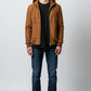 Scarlett Stitch brown suede bomber jacket with detachable hood, zip closure, and ribbed cuffs. Model wears black t-shirt and blue jeans.